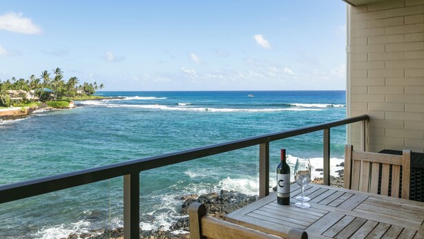 A wooden table with a bottle and glass on a balcony overlooking the ocean. - Live On the Ocean and Sleep to Surf Sounds in Idyllic Poipu. Trade Winds & AC.
 (Poipu)