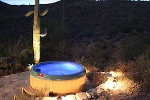 A hot tub in a desert setting with a wooden deck and a stone fire pit. - Sahuaro Ranch Hideaway (Tucson)