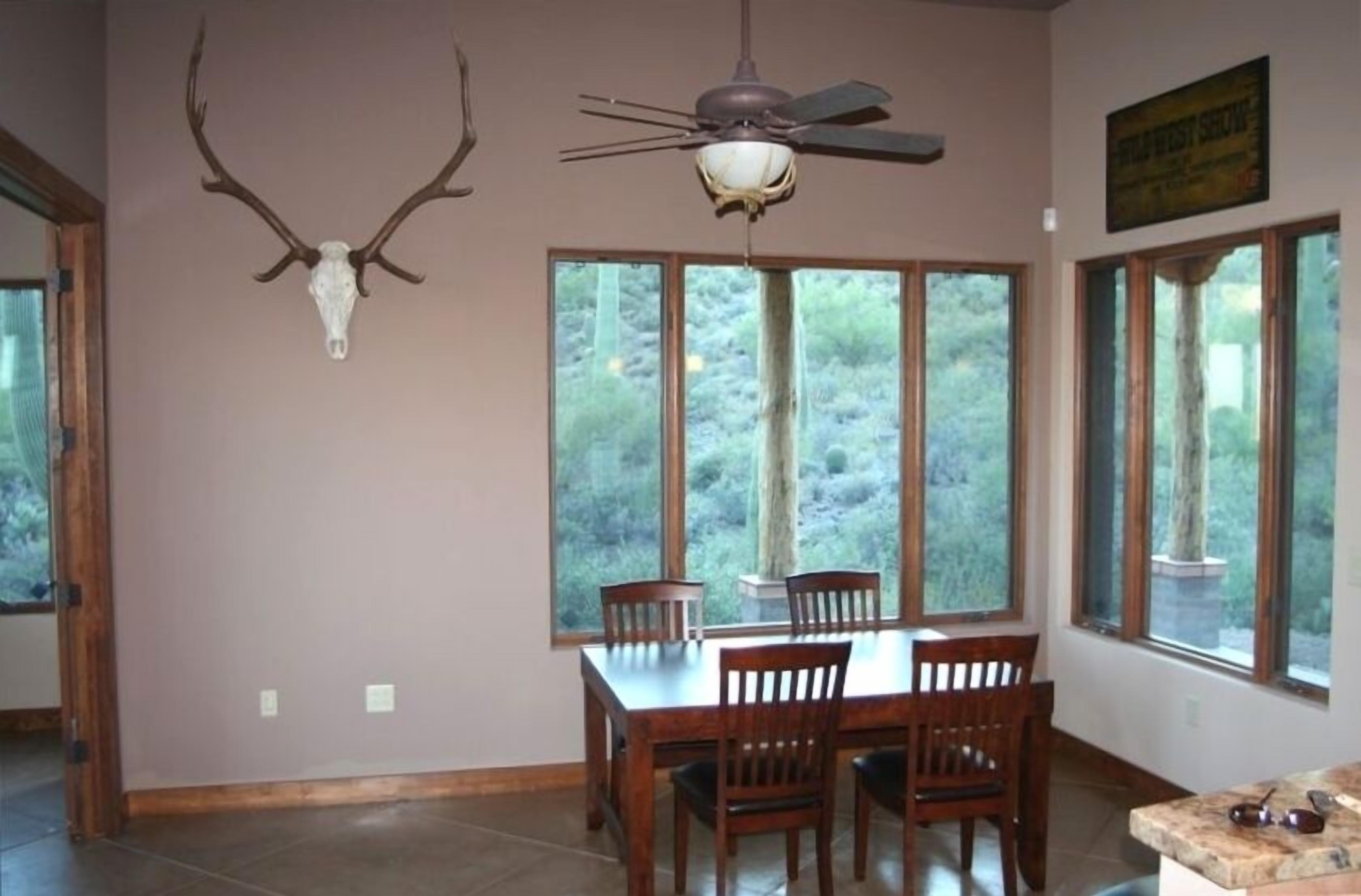 A dining area with a table and chairs, a ceiling fan, and a large window with a view of trees.