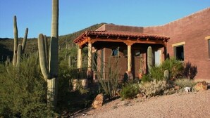 A rustic building with a red-tiled roof and a wooden porch, surrounded by cacti and shrubs. - Sahuaro Ranch Hideaway (Tucson)