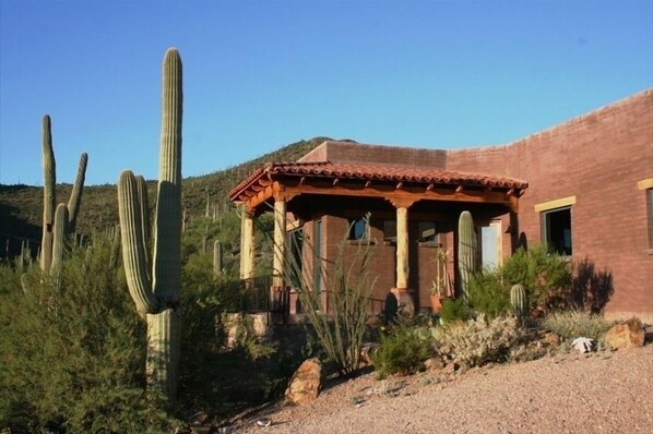 A rustic building with a red-tiled roof and a wooden porch, surrounded by cacti and shrubs. - Sahuaro Ranch Hideaway (Tucson)