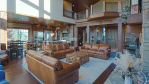 A spacious living area with leather sofas, a stone fireplace, and a balcony overlooking the landscape. - Spring Shores Lodge - Luxury mountain estate on a private lake. With 3 en-suite king bedrooms 4 other bedrooms and 2 large bunkrooms, it sleeps up to 40 guests—perfect for family reunions, retreats, and group getaways in a secluded luxury setting. (Ashton)