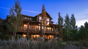 A large, multi-story wooden house with multiple balconies and large windows, surrounded by tall trees and overgrown vegetation. - Spring Shores Lodge - Luxury mountain estate on a private lake. With 3 en-suite king bedrooms 4 other bedrooms and 2 large bunkrooms, it sleeps up to 40 guests—perfect for family reunions, retreats, and group getaways in a secluded luxury setting. (Ashton)