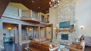 A spacious living area with a stone fireplace, leather sofas, and a wooden bench. - Spring Shores Lodge - Luxury mountain estate on a private lake. With 3 en-suite king bedrooms 4 other bedrooms and 2 large bunkrooms, it sleeps up to 40 guests—perfect for family reunions, retreats, and group getaways in a secluded luxury setting. (Ashton)