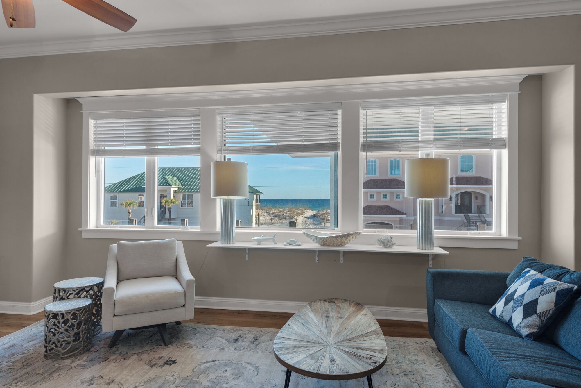 A living room with a view of the beach, a sofa, a chair, and decorative items on a windowsill.
