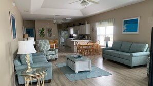 A spacious living room with a blue sofa, a glass coffee table, and a dining area with wooden chairs. - Oh the views, hear the surf Great location all year long (Gulf Shores)