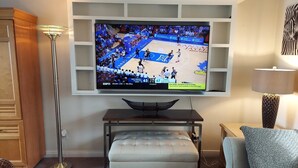 A living room with a flat-screen TV mounted on a wall, a white ottoman, a floor lamp, and a couch. - Luxury Townhouse at the Gateway to the Utah Canyons, Best Price On VRBO! (Cottonwood Heights)