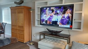 A living room with a flat-screen TV mounted on the wall, a wooden cabinet, a leopard-print sofa, and a white cushioned bench. - Luxury Townhouse at the Gateway to the Utah Canyons, Best Price On VRBO! (Cottonwood Heights)