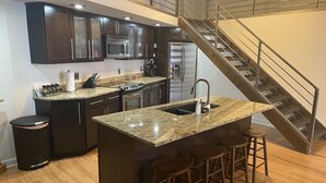 Une cuisine moderne avec des meubles de couleur sombre, des plans de travail en granit et un îlot central doté de tabourets de bar.
