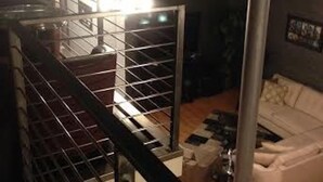 Un escalier avec une rampe en métal mène à un espace de vie comprenant un canapé blanc et une table basse.