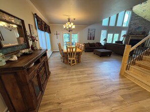 A spacious living area with a dining table, wooden chairs, a sofa, and a staircase. - Hidden River Lodge, Beautiful And Spacious River Front Home, Sleeps 15 (South Fork)
