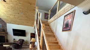 Una escalera de madera con barandilla, un televisor de pantalla plana en la pared, una chimenea y una zona de estar con sofá y mesa.
