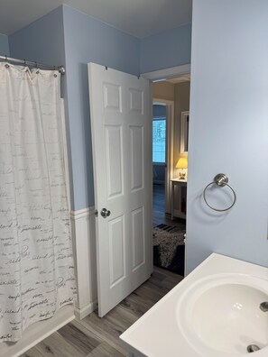 Une salle de bain avec un lavabo blanc, un rideau de douche orné de motifs textuels et une porte donnant sur une autre pièce.