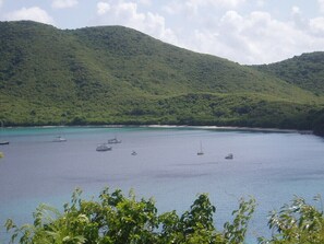 Un paisaje costero con una bahía, barcos y una colina boscosa.