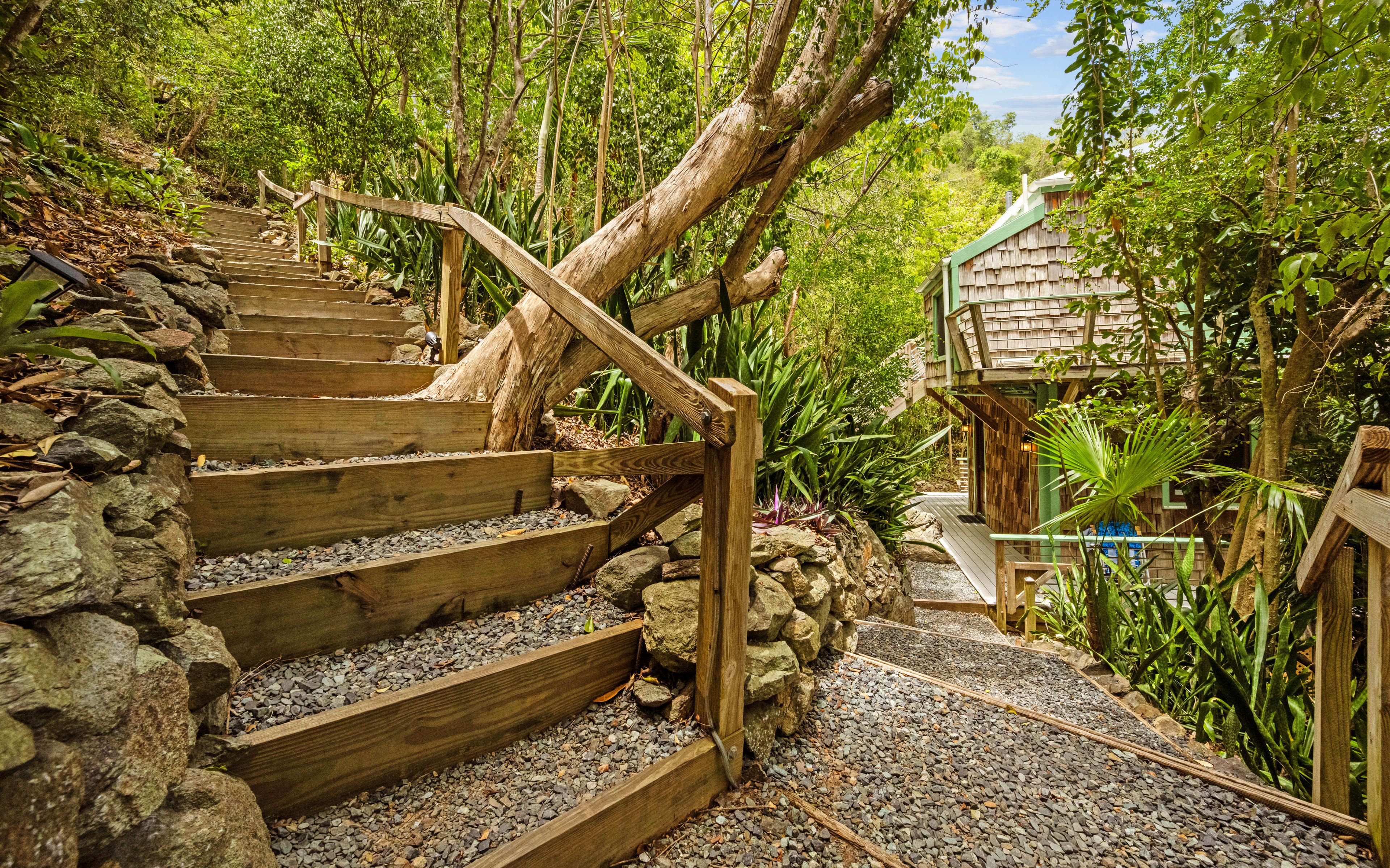 A wooden staircase with stone steps leading up to a wooden structure surrounded by lush greenery.