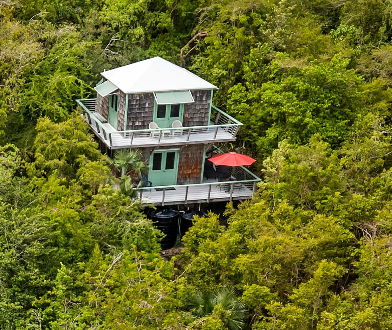 A two-story wooden structure with a balcony, surrounded by dense greenery.