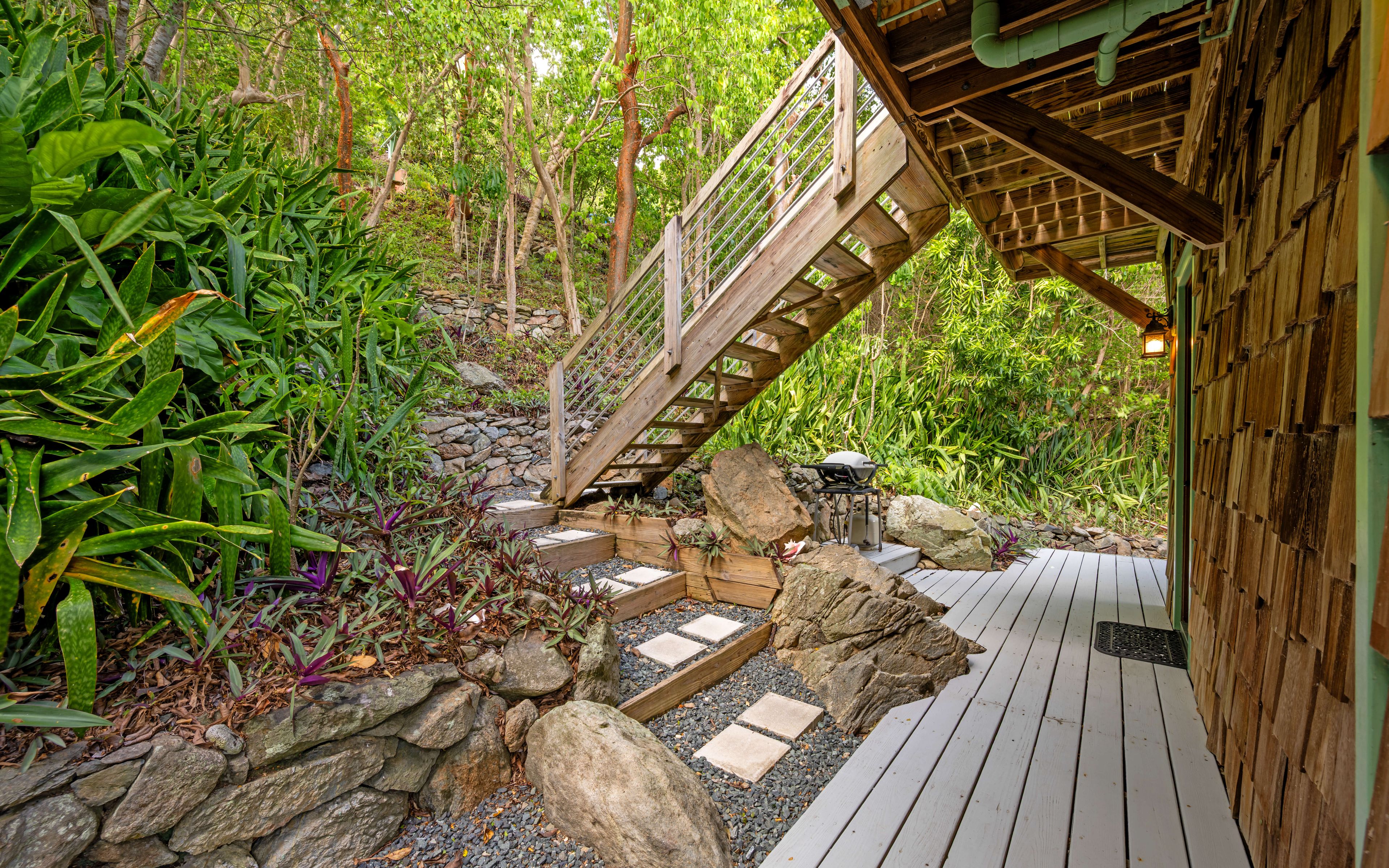 A wooden deck with a stone pathway leading to a wooden staircase.