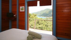 Ein Schlafzimmer mit Bett, Fernseher und einem Balkon mit Blick auf ein Tal und Berge.