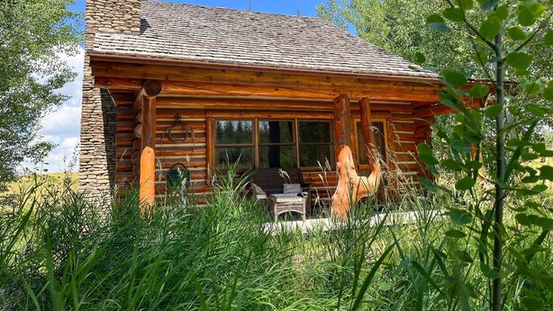 Eine rustikale Holzhütte mit einem Steinkamin, großen Fenstern und einer Veranda mit Sitzgelegenheiten.