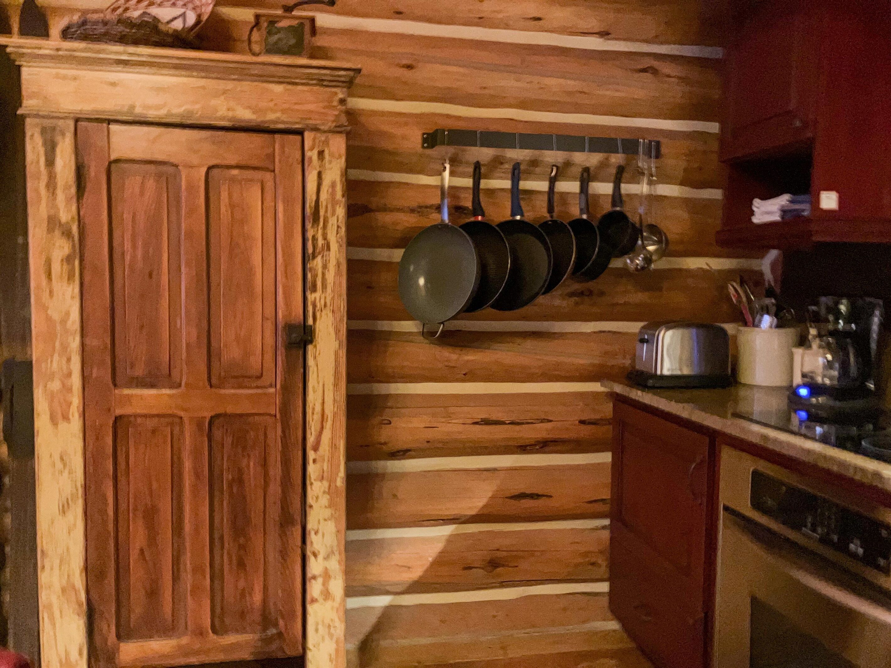 Een rustieke keuken met houten wanden, een houten deur en een hangende kruidenrek.