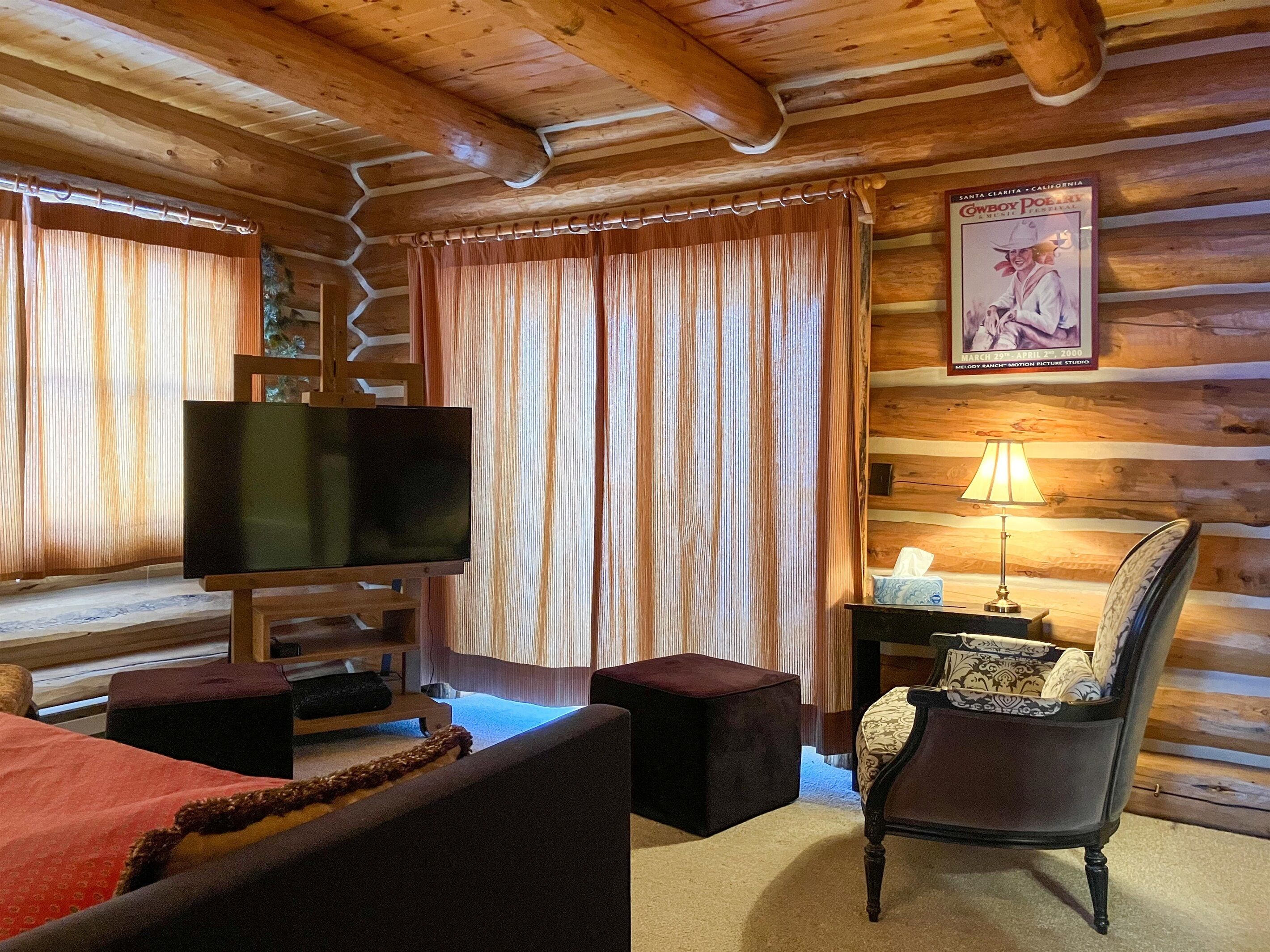 Interior de una cabaña de madera con televisión, lámpara, una silla y un cartel en la pared.
