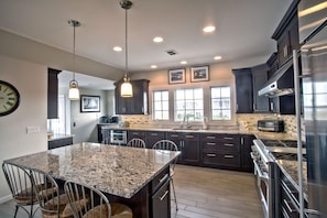 A modern kitchen with granite countertops, stainless steel appliances, and a dining area with a marble table and metal chairs. - Great Views. Only Steps From the Beach. (Long Beach Township)
