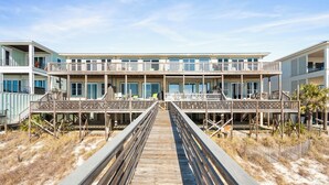 A wooden boardwalk leading to a beachfront building with multiple balconies and outdoor seating areas. - Rammer Jammer-Gulf Front Home with Private Beach Crossover (Navarre)