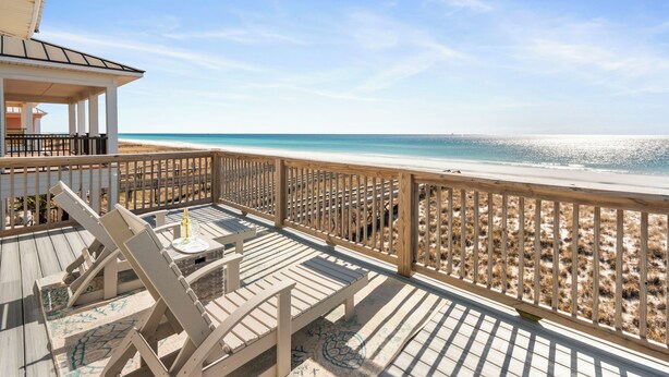 A wooden deck with lounge chairs and a small table, overlooking a beach with a sandy shore and clear blue water. - Rammer Jammer-Gulf Front Home with Private Beach Crossover (Navarre)