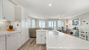 A modern kitchen with white cabinetry, a central island, and a view of the ocean. - Rammer Jammer-Gulf Front Home with Private Beach Crossover (Navarre)
