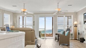 A spacious living area with a large sliding glass door leading to a balcony with a view of the ocean. There are two ceiling fans, a sofa, and a wicker chair. - Rammer Jammer-Gulf Front Home with Private Beach Crossover (Navarre)