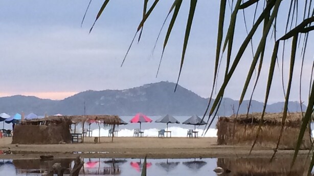 Un lago tranquilo que refleja una cadena montañosa y una cabaña con techo de paja.