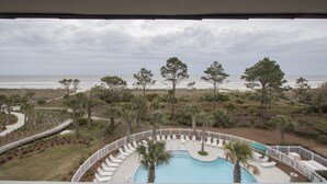 Ett poolområde med solstolar och utsikt över stranden och havet.