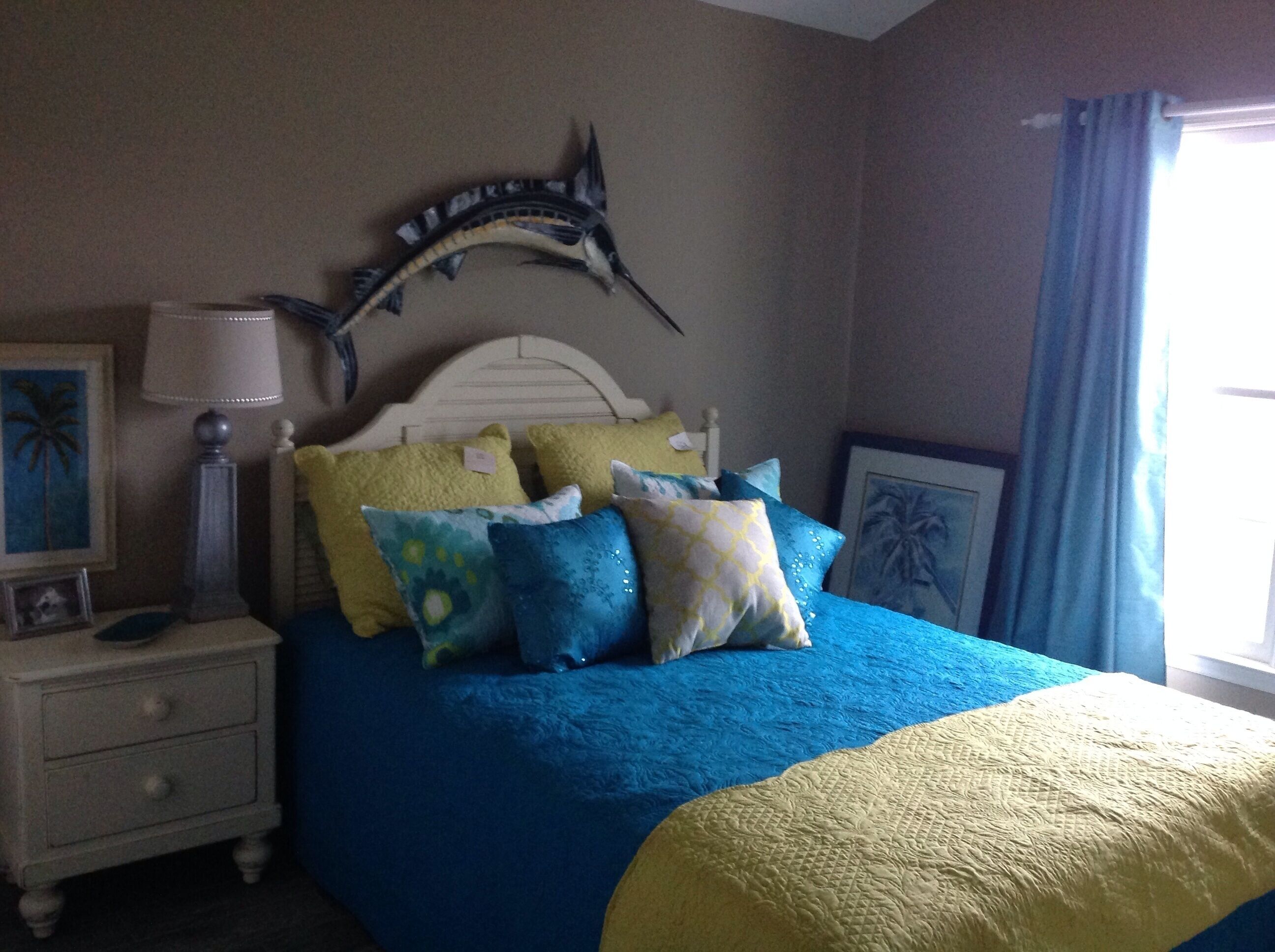 Een slaapkamer met een bed, nachtkastje, lamp en een decoratie aan de muur.