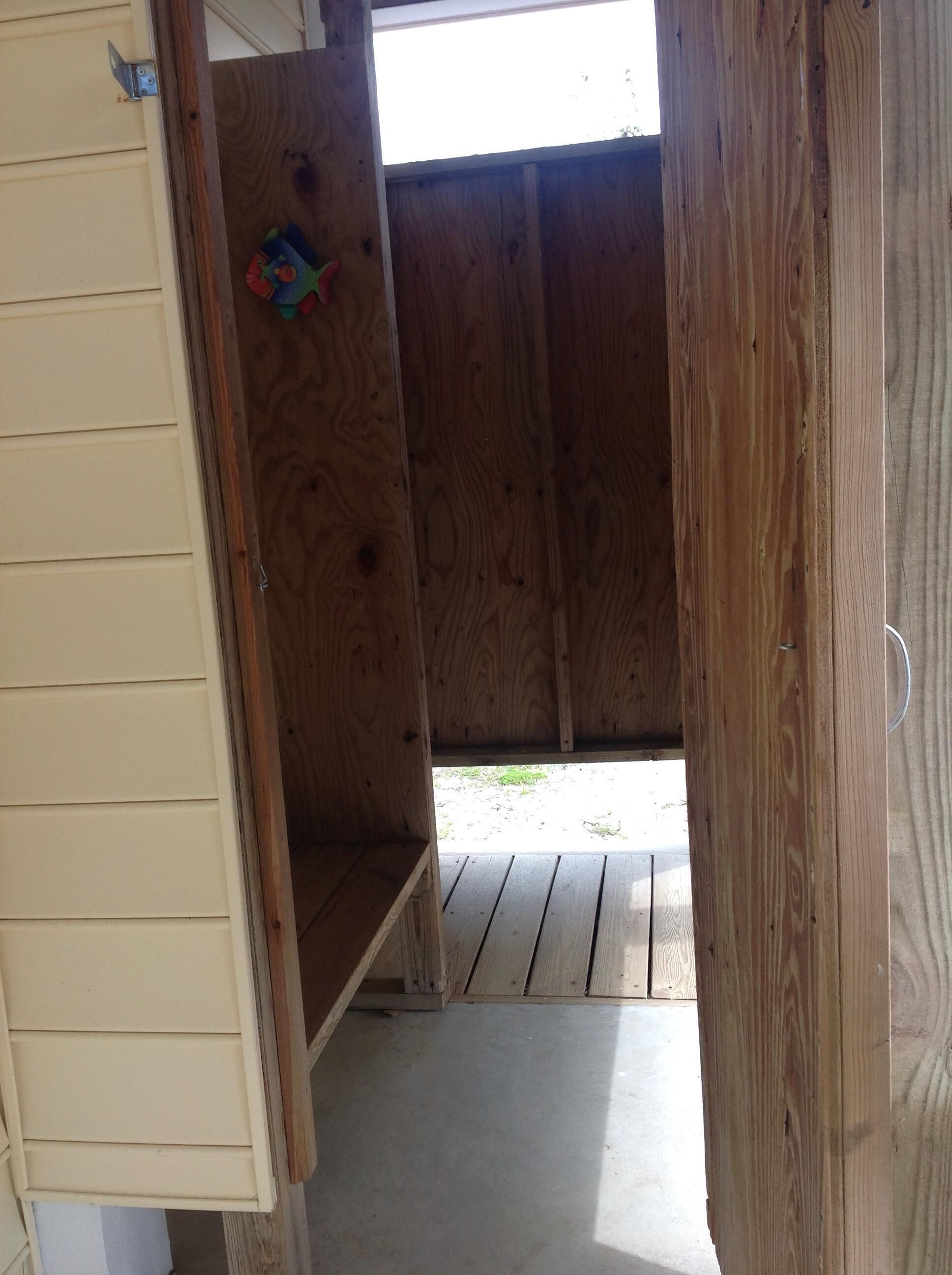 A wooden shed with a door open, revealing a concrete floor and a grassy area outside.