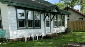Ein Haus mit grüner Dachbegrünung und weißer Fassade, eine Veranda mit weißen Stühlen und ein kleiner Garten.