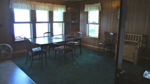 Ein Esszimmer mit Holztisch und -stühlen, großen Fenstern mit Vorhängen und einem Deckenventilator.