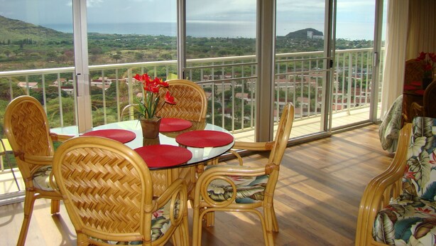 A balcony with wicker furniture, a table with red cushions, and a view of a coastal landscape. - Affordable Luxury, Gorgeous One Bedroom Condo, Amazing Views and Great WiFi (Waianae)