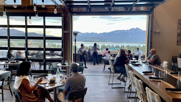 A restaurant with large windows offering mountain views, multiple tables, and chairs arranged for dining. - Lake Dillon Condominium with Beautiful Lake & Mountain Views. Sleeps 4. (Dillon)
