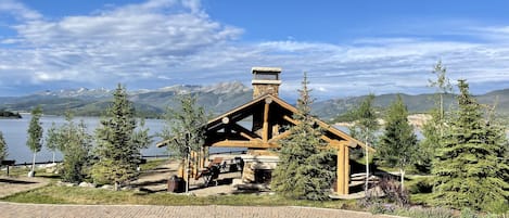 Een lodge met een stenen schoorsteen, houten balken en uitzicht op een meer en bergen.