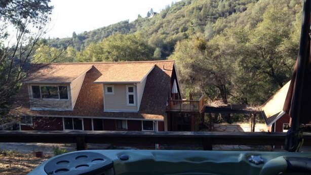 A hot tub with a wooden deck and a view of a house with a sloped roof and a balcony. - Charming Creekside Country Home (Sutter Creek)