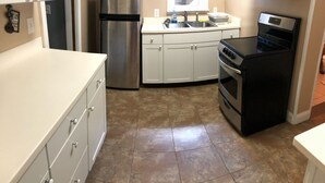 A kitchen with white cabinets, a stainless steel refrigerator, a black stove, and a window above the sink. - 1st Class Rentals 2 Bedroom Downstairs Apartment. (Oneonta)