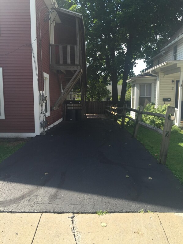 A residential driveway leading to a two-story house with a visible garage door and a wooden fence. - 1st Class Rentals 2 Bedroom Downstairs Apartment. (Oneonta)