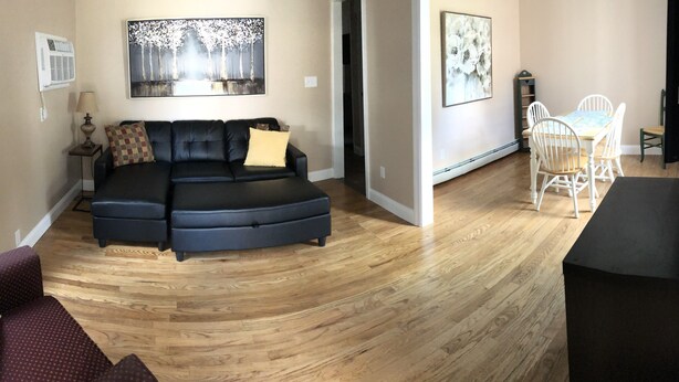 A living room with a sectional sofa, a dining area with a table and chairs, and artwork on the walls. - 1st Class Rentals 2 Bedroom Downstairs Apartment. (Oneonta)