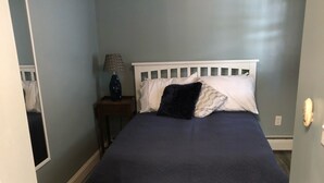 A bedroom with a white bed frame, dark blue bedding, and a wooden floor. - 1st Class Rentals 2 Bedroom Downstairs Apartment. (Oneonta)