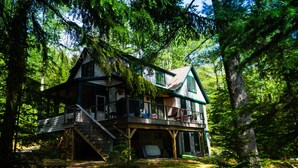 A cabin with a balcony, surrounded by dense forest.