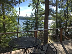 Une terrasse avec une table et des chaises en métal, donnant sur un lac entouré d’arbres.