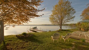 A lakeside deck with lounge chairs, a grill, and a dock extending into the water.