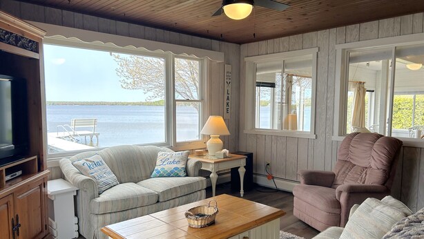 A cozy living room with a view of a lake, featuring a sofa, armchair, and a wooden coffee table.