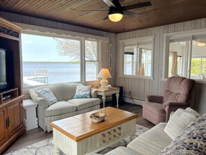 A cozy living room with a view of a lake, featuring a sofa, armchair, and a wooden coffee table.