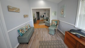 Un couloir avec un canapé gris, un pouf assorti et un meuble en bois orné d’un motif de poisson décoratif.